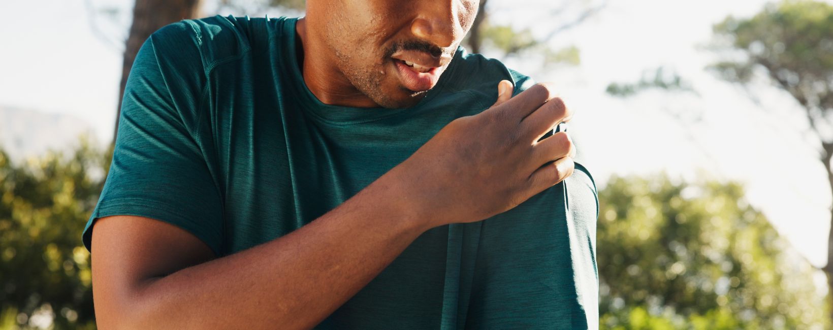 Man experiencing shoulder impingement symptoms while outdoors holding painful shoulder area
