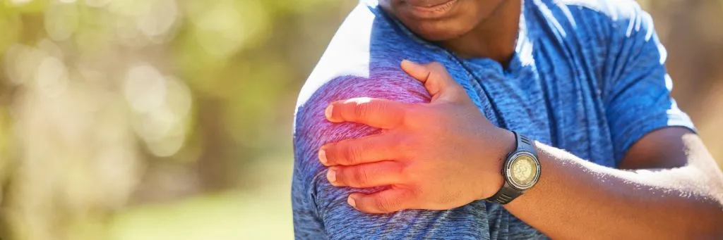 Athletic man in blue shirt holding painful shoulder outdoors during shoulder surgery recovery demonstrating common recovery challenges and the importance of proper post-operative care